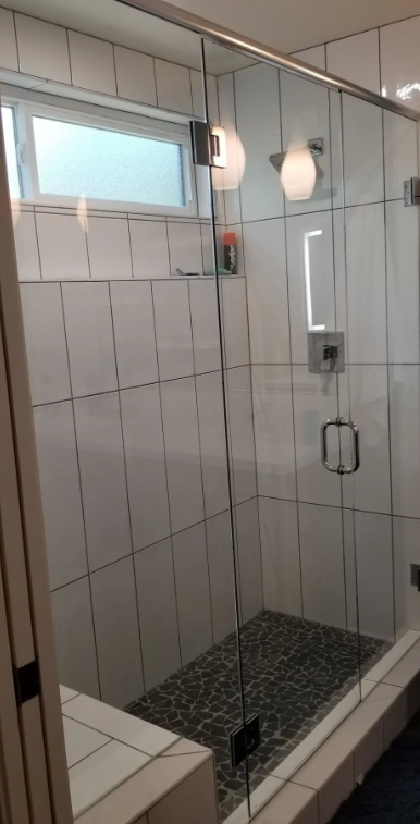 Frameless glass shower enclosure with white subway tile and pebble floor in Madera, CA